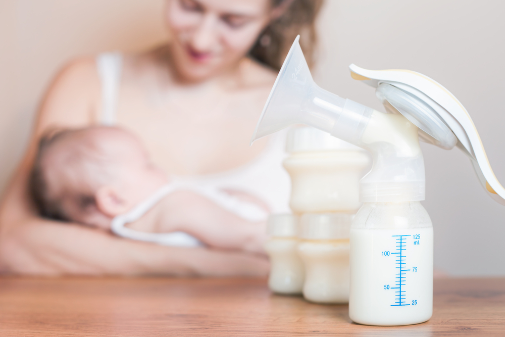 Manual breast pump with breast milk, mother and baby in the background