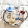 All four Happy Cappy routine products arranged in a towel-lined basket: Medicated Wash, Daily Wash, cream tube, and cream pump jar