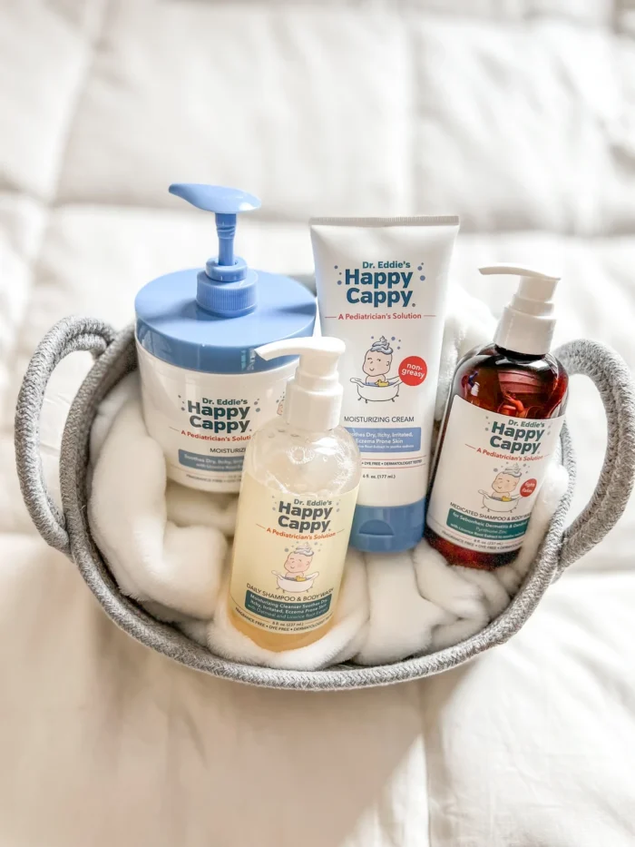 All four Happy Cappy routine products arranged in a towel-lined basket: Medicated Wash, Daily Wash, cream tube, and cream pump jar