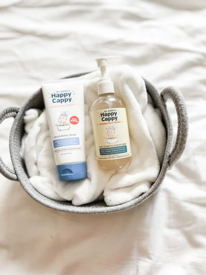 Happy Cappy Daily Shampoo and Body Wash and 6 oz Moisturizing Cream tube in a basket with a white bath towel