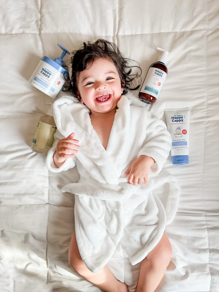 A smiling child in a white bathrobe with Happy Cappy skin and scalp care products.