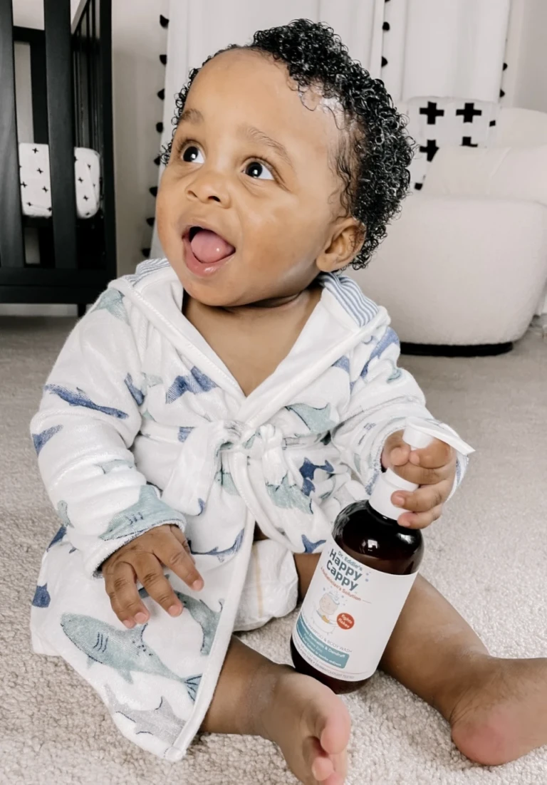 A delighted toddler in a patterned robe holding Happy Cappy Medicated Shampoo & Body Wash