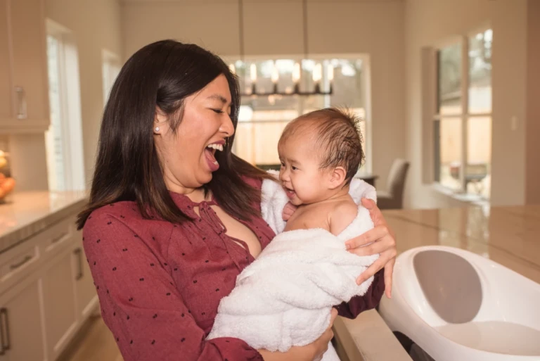 A mother smiling at her baby wrapped in a white towel after a bath
