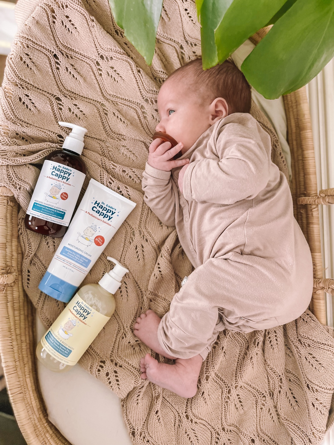Baby in a pink outfit beside Happy Cappy skin and scalp care products.