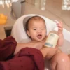 Baby in a bath seat holding a bottle of Happy Cappy daily shampoo and body wash