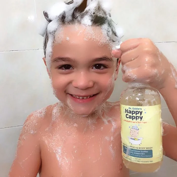 Smiling boy covered in lather holding the Happy Cappy daily shampoo and body wash