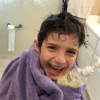 Laughing boy wrapped in a towel with wet hair holding the daily wash bottle