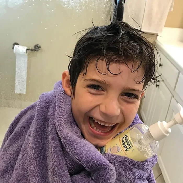 Laughing boy wrapped in a towel with wet hair holding the daily wash bottle