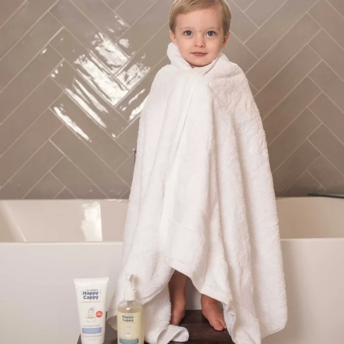 Toddler wrapped in a towel beside Happy Cappy daily wash and moisturizing cream