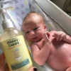 Hand holding the daily wash bottle beside a newborn resting in a bath seat