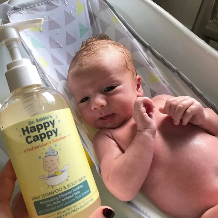 Hand holding the daily wash bottle beside a newborn resting in a bath seat
