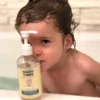 Toddler in the bath beside the Happy Cappy daily wash pump bottle
