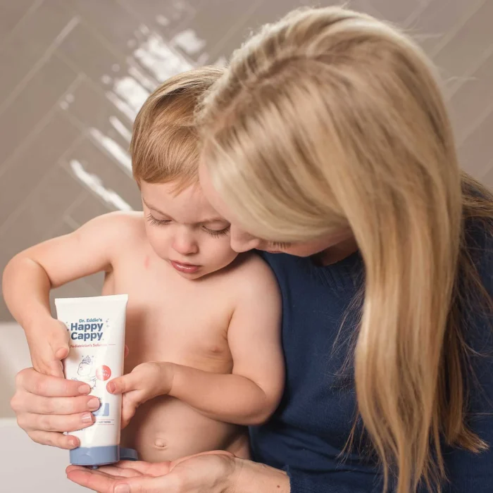 Toddler squeezing Happy Cappy moisturizing cream from the tube with a parent