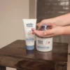 Hands pumping Happy Cappy moisturizing cream from the 12 oz jar next to the tube