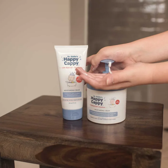 Hands pumping Happy Cappy moisturizing cream from the 12 oz jar next to the tube